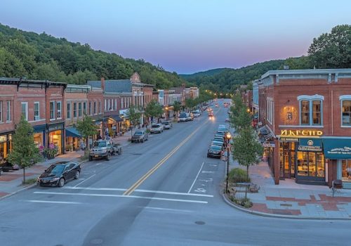charming-small-town-street-dusk-cars-parked-along-side-shops-buildings-with-lights_1124373-2545